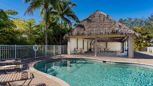 A swimming pool with lounge chairs, a thatched-roof structure, and a fenced area. - ~the Bonita Paddle Efficiency~ Your Home Away From Home In Paradise 1 Bedroom Condo by RedAwning (Bonita Springs)