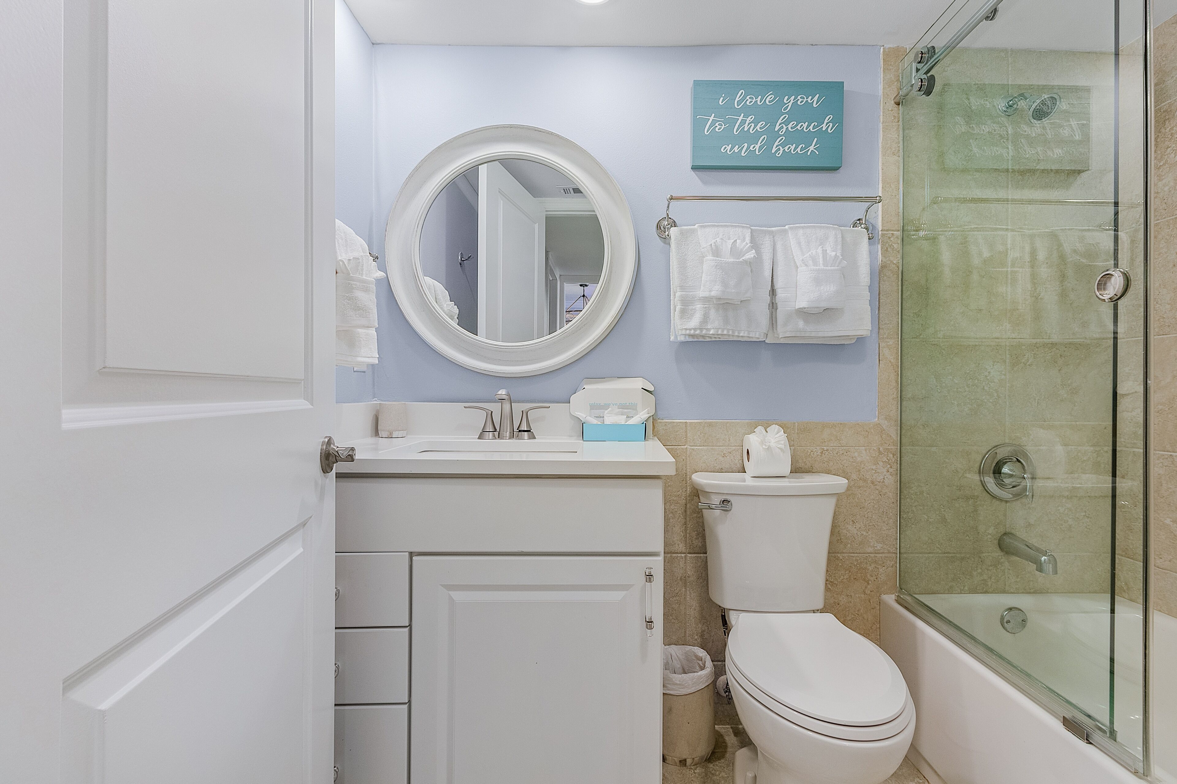 Un baño con inodoro, lavabo, espejo y ducha con mampara de vidrio.