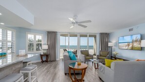 A spacious living area with a view of the ocean, a ceiling fan, and a television on the wall.