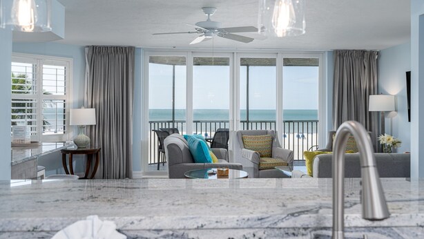 A spacious living room with a large window offering a view of the sea, a ceiling fan, and a marble floor.