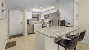 A modern kitchen with white cabinets, a granite countertop, a stainless steel refrigerator, and a microwave.