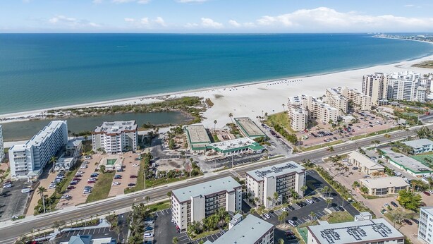 A coastal cityscape with a beachfront, high-rise buildings, and a parking area.
