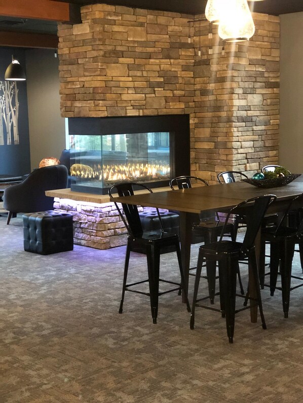 A dining area with a stone fireplace, a round table, and black chairs. - The Lodge at Wisp Resort (McHenry)