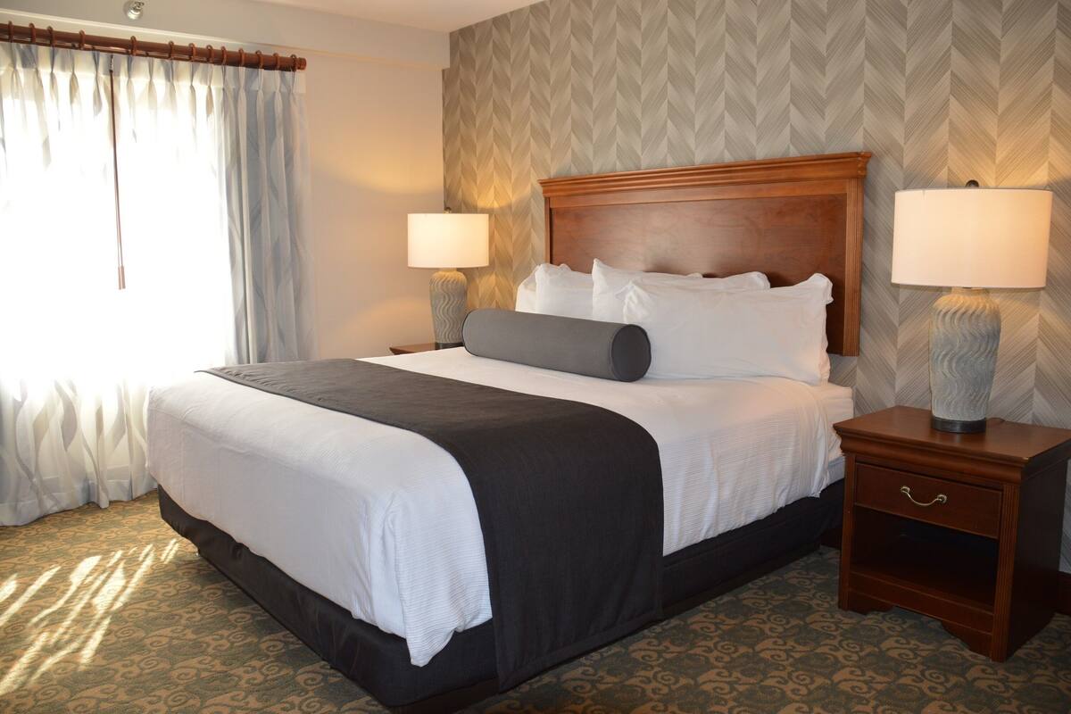 A neatly made bed with a wooden headboard, two bedside lamps, and a nightstand with a drawer.