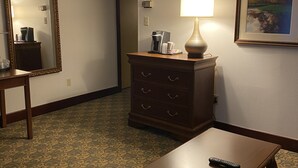 Habitación de hotel con alfombra estampada, cómoda de madera con lámpara, cuadro en la pared y control remoto sobre una mesa.