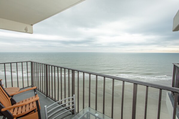 A balcony with a view of the ocean, equipped with wooden chairs and a glass table. - Royal Garden Resort 1114 2 Bedroom Condo by RedAwning (Murrells Inlet)