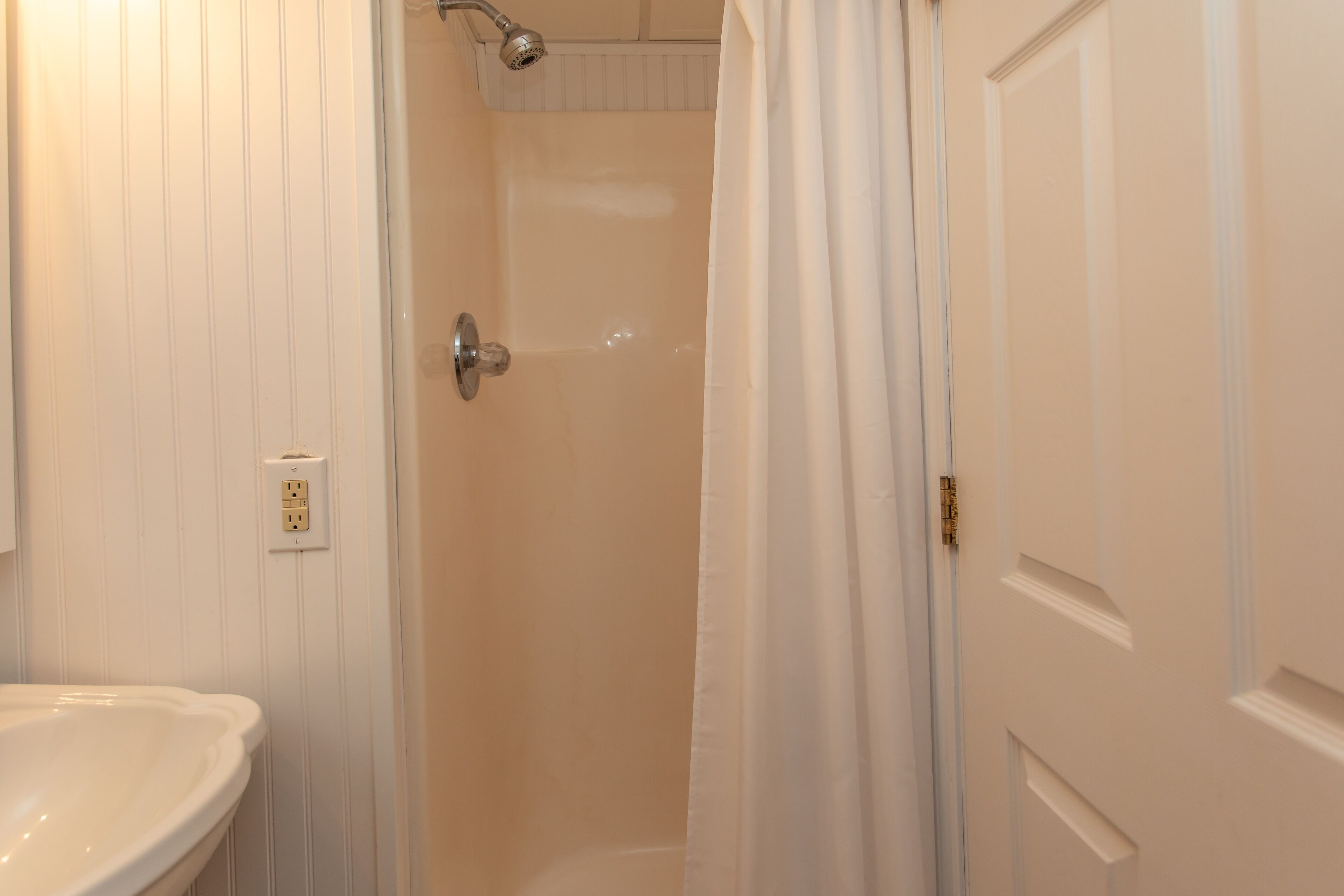 Un baño con un lavamanos blanco, una ducha con cortina y una puerta con pomo.
