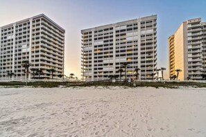 Un hotel frente a la playa con varios edificios altos, que cuenta con balcones y una playa de arena en primer plano.
