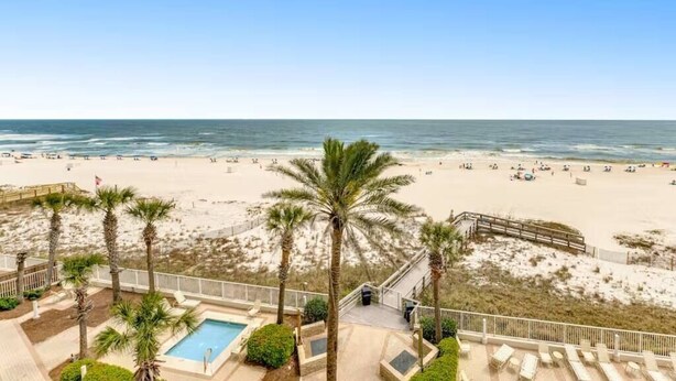 A beach view with a pool, palm trees, and a wooden deck. - Pelican Pointe|Beachfront|Gulf Views|Indoor Pool (Orange Beach)