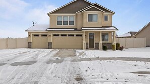 A two-story house with a garage, a front porch, and a snow-covered driveway. - Modern Family Friendly House (Kennewick)