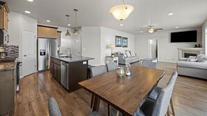 A modern kitchen with a central island, a dining area with a wooden table, and a living room with a sofa and TV. - Modern Family Friendly House (Kennewick)
