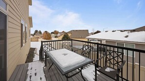 A deck with a table and chairs, surrounded by a metal railing, overlooking a residential area with houses and a clear sky. - Modern Family Friendly House (Kennewick)