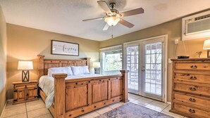 A bedroom with a wooden bed, a ceiling fan, a nightstand with a lamp, a dresser, and a window with blinds. - Lakefront Home w/ Point Venture Golf Access! (Point Venture)
