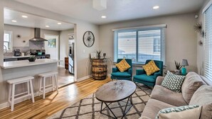 A modern living room with a sofa, a coffee table, and two armchairs. A kitchen area with a bar and stools is visible in the background. - Grand Junction Vacation Rental w/ Fire Pit! (Grand Junction)
