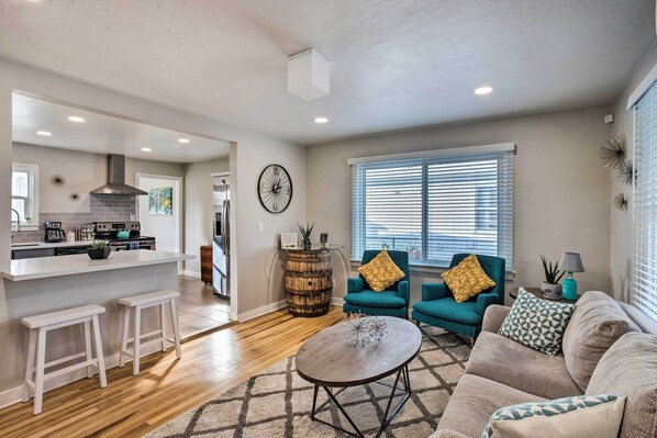 A modern living room with a sofa, a coffee table, and two armchairs. There is a kitchen area with a bar and stools.