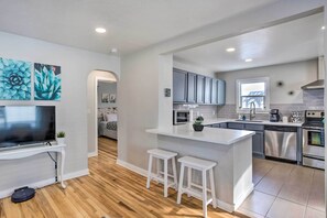 A modern kitchen with a central island, stainless steel appliances, and a flat-screen TV on a white console.