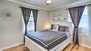 A bedroom with a bed, ceiling fan, window with curtains, and a decorative wall piece. - Grand Junction Vacation Rental w/ Fire Pit! (Grand Junction)