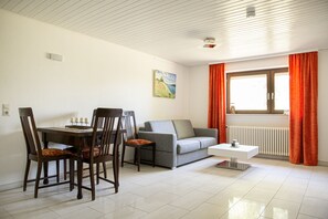 A living room with a dining table, chairs, a sofa, a coffee table, and a window with curtains.