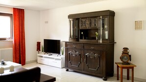 Ein Wohnzimmer mit Fernseher, Schrank, kleinem Tisch und einer Uhr.