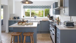 Une cuisine moderne dotée d’un grand îlot central, d’appareils électroménagers intégrés et d’une fenêtre donnant sur un espace verdoyant.