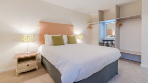 Une chambre à coucher avec un grand lit, deux tables de chevet, une commode, une fenêtre donnant sur un beau paysage et une armoire.