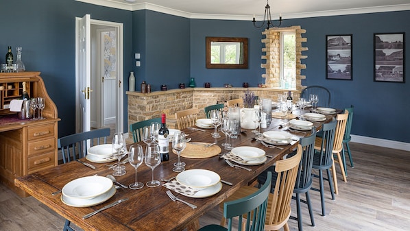 Ein Esszimmer mit einem langen Holztisch, gedeckt für eine Mahlzeit, umgeben von Stühlen.