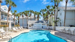 A swimming pool surrounded by palm trees and lounge chairs, with a clear blue sky above. - Destin Crystal Beachside Escape~Steps to Beach & Pool~Prime location (Destin)