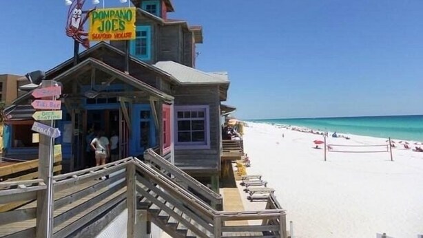 A beachside building with a sign reading "Dompano Joes" and multiple directional signs. - Destin Crystal Beachside Escape~Steps to Beach & Pool~Prime location (Destin)