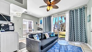A modern living room with a grey sofa, a ceiling fan, and a view of the outdoors. - Destin Crystal Beachside Escape~Steps to Beach & Pool~Prime location (Destin)