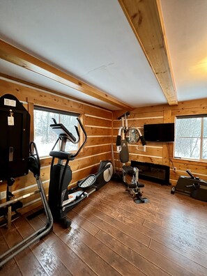 Eine Holzhütte mit Fitnessbereich, ausgestattet mit einem Crosstrainer, einem stationären Fahrrad und einem Laufband.