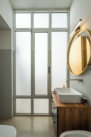 Ein modernes Badezimmer mit einer großen Milchglasschiebetür, einem runden Spiegel, einem weißen Waschbecken und einer Holzkommode.