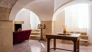 Una habitación con un sofá de terciopelo rojo, una mesa de madera con velas y un cuadro sobre un caballete.