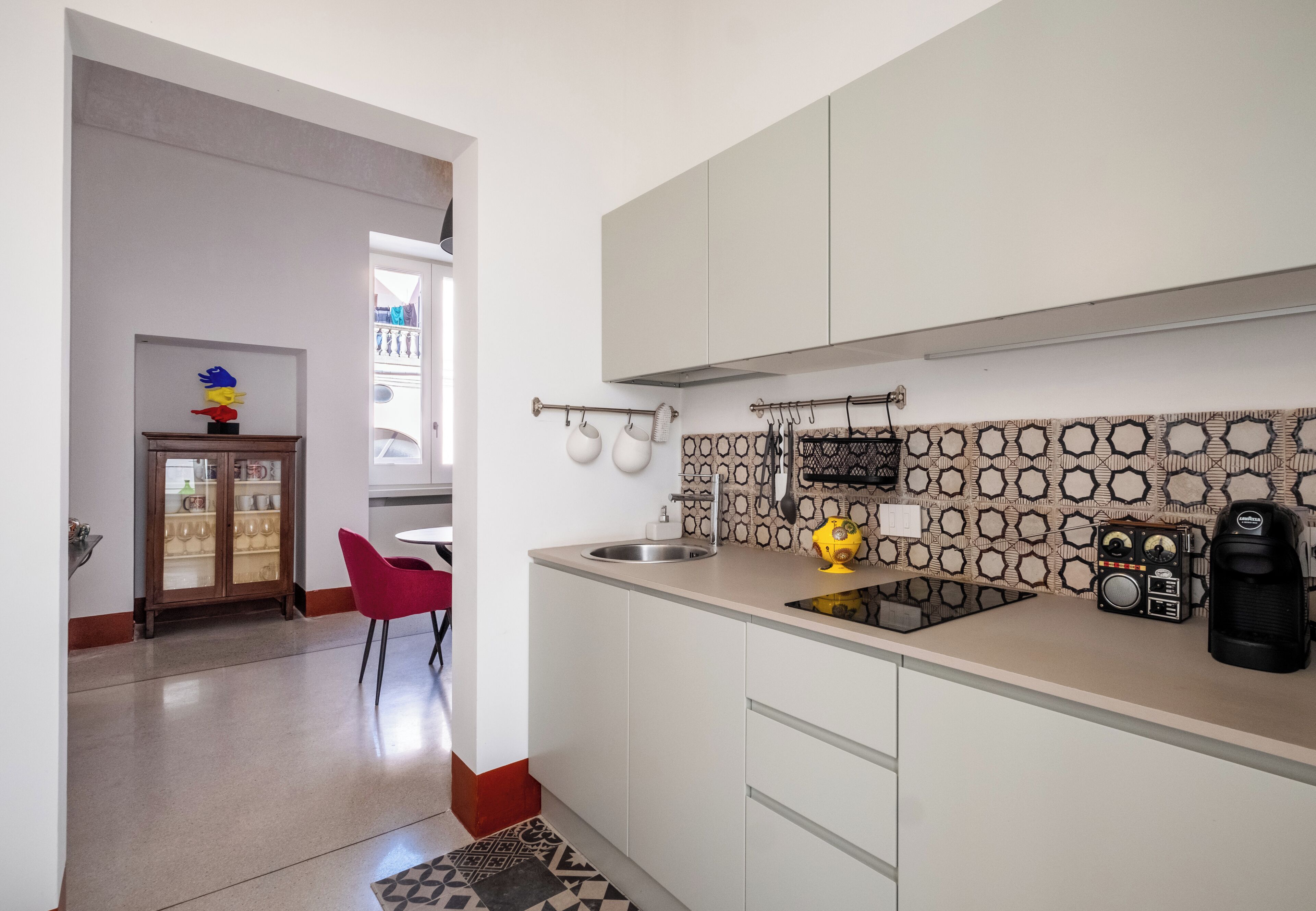 A modern kitchen with white cabinets, a patterned backsplash, a coffee machine, and a red chair.