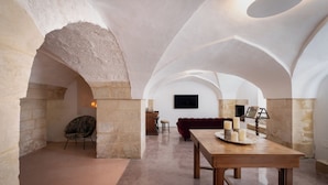Un interior espacioso con techos altos en arco y paredes de piedra, que incluye una mesa de madera con velas y un sofá rojo.