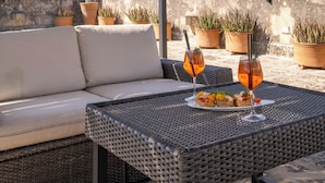 Una terraza en la azotea con una mesa de mimbre para dos personas, un sofá y plantas en macetas.