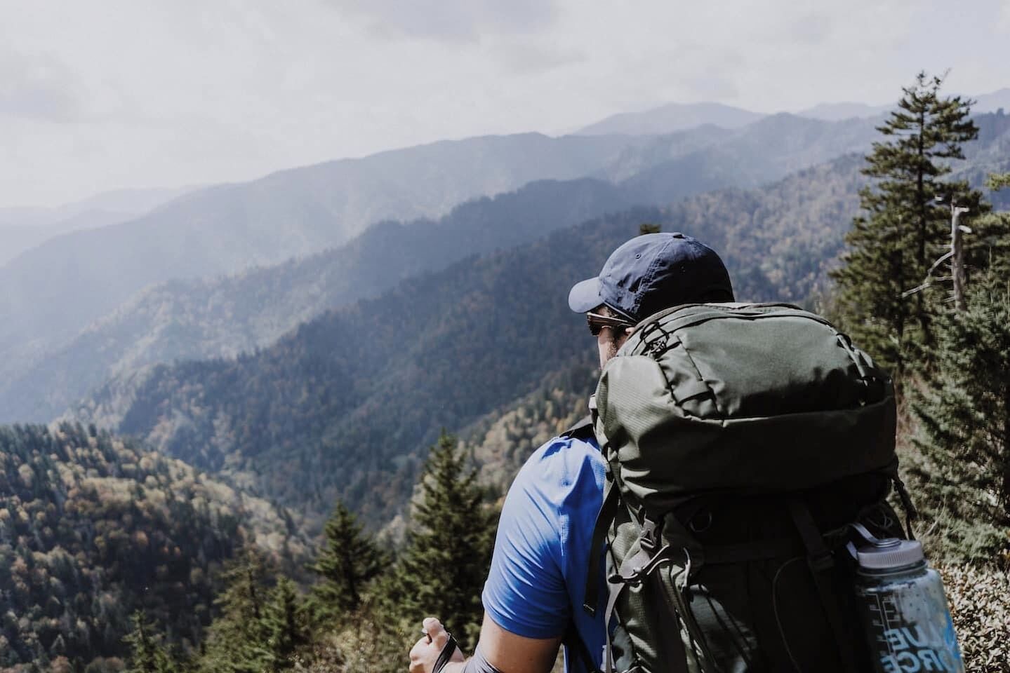 A hiker with a backpack and water bottle, overlooking a mountainous landscape.