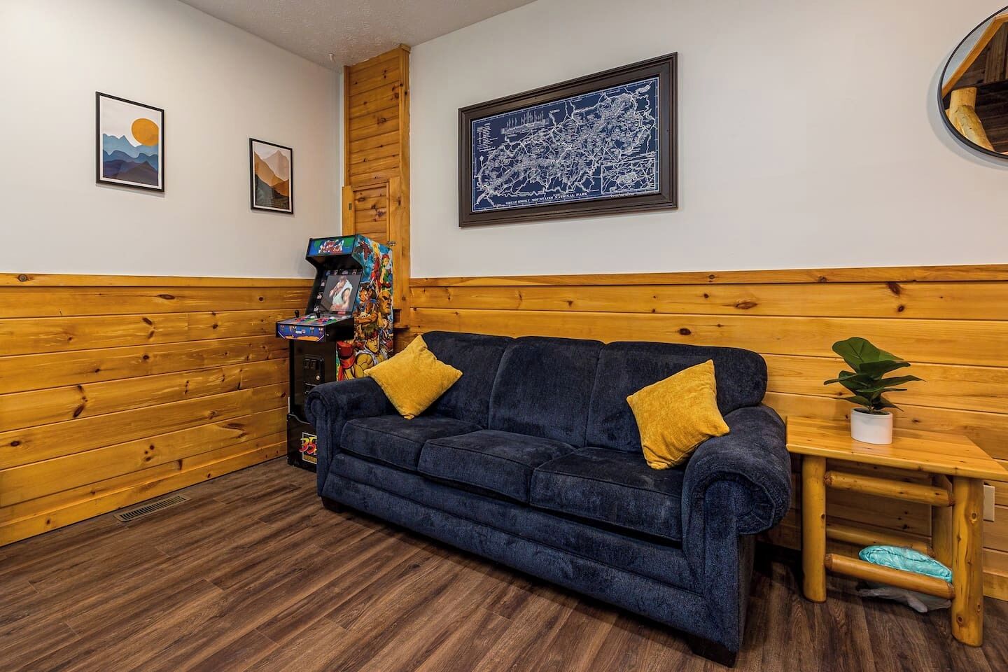 A room with a dark blue sofa, wooden panel walls, a framed map, and a small table with a plant.