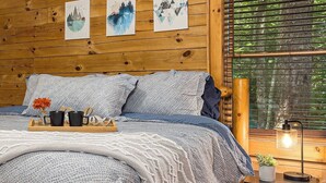 Una habitación de madera con una cama, obras de arte en la pared y una ventana con persianas.