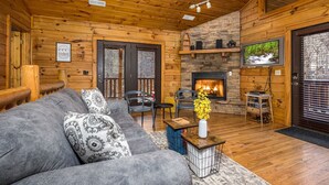 Interior de una cabaña de madera con chimenea, un sofá y un televisor.