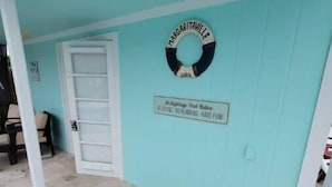 Une pièce avec un mur bleu clair, une porte blanche, un tapis coloré et une enseigne sur laquelle on peut lire « Margaritaville ».