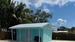 Une piscine avec un patio couvert, une clôture en bois et des palmiers en arrière-plan.