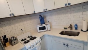 Une cuisine de taille réduite avec des meubles blancs, un four à micro-ondes, une cuisinière et un évier.
