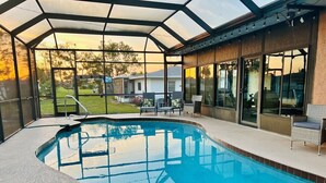 A swimming pool with a glass enclosure, surrounded by patio furniture and a view of the backyard. - Only 2.5 miles to Beach + Heated Saltwater Pool Included! (Englewood)