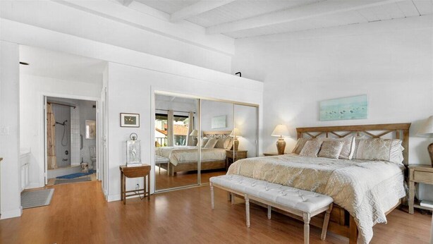 A spacious bedroom with a large bed, a bench, a mirror, and a view of the outside. - Carlsbad Hideaway. Pool, Spa, BBQ. Walking to restaurants/shops (Carlsbad)