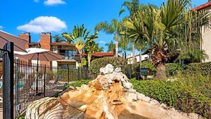 A pool area with a rocky water feature, surrounded by palm trees and a fence. - Carlsbad Hideaway. Pool, Spa, BBQ. Walking to restaurants/shops (Carlsbad)