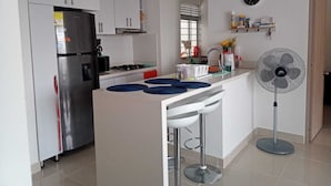 A modern kitchen with white cabinets, a stainless steel refrigerator, a gas stove, and a bar area with stools.