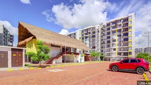 A modern building with a thatched-roof structure, a red car, and a multi-story residential building in the background.