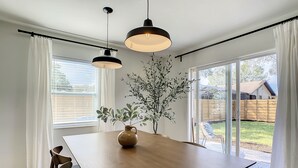 A dining area with a wooden table, two pendant lights, a vase with greenery, and a view of a backyard through large sliding glass doors. - Cypress Inn - Modern home close to Siesta Key (Sarasota)