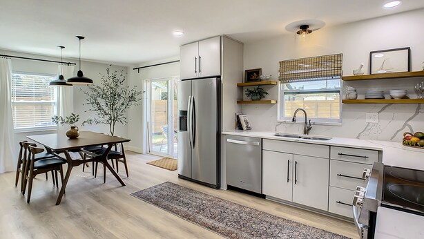 A modern kitchen with a dining area, featuring a stainless steel refrigerator, wooden dining table, and pendant lighting. - Cypress Inn - Modern home close to Siesta Key (Sarasota)