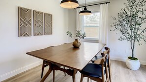 A dining area with a wooden table, chairs, pendant lights, wall art, and a potted plant. - Cypress Inn - Modern home close to Siesta Key (Sarasota)